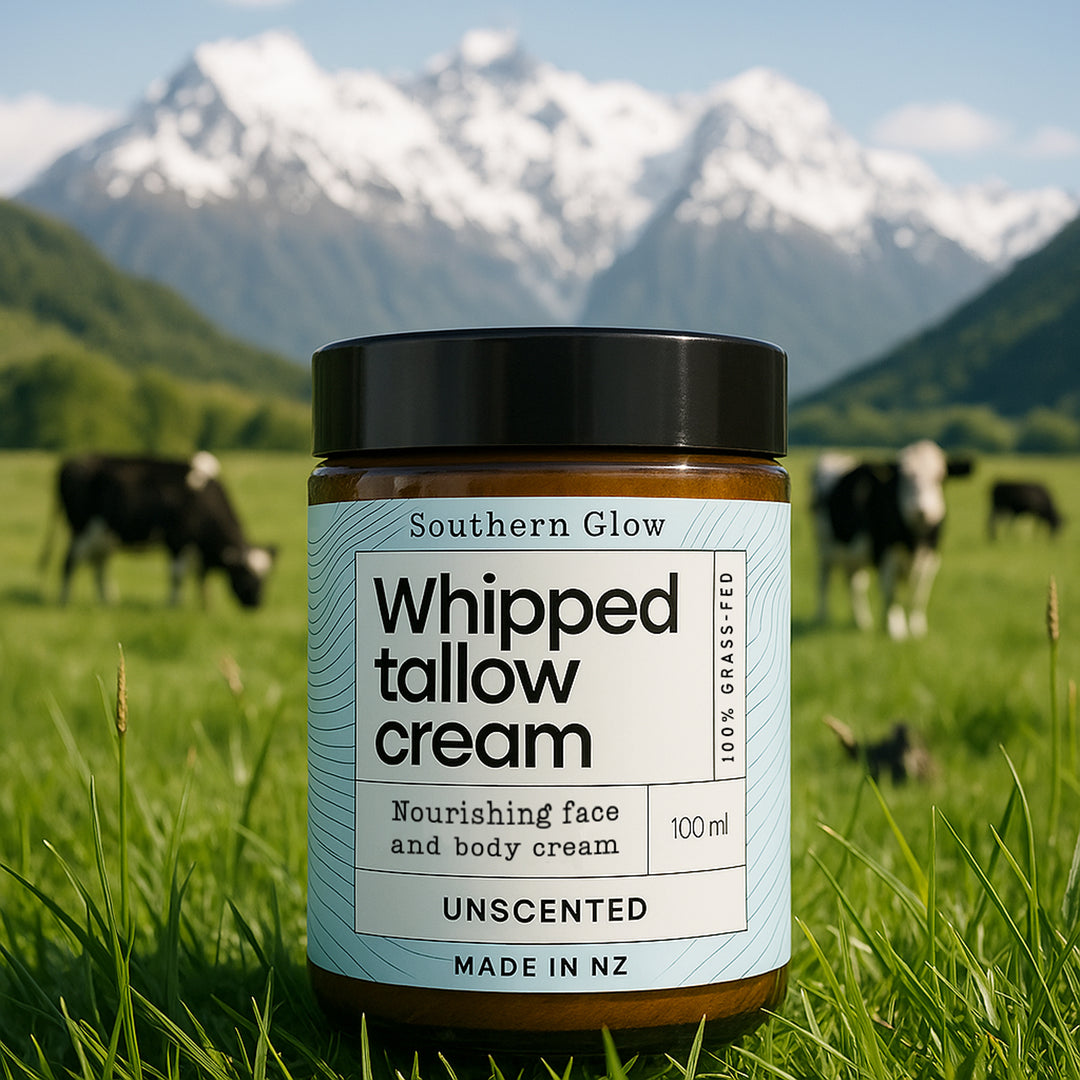 Jar of whipped tallow cream in a grassy field with cows and mountains in the background.