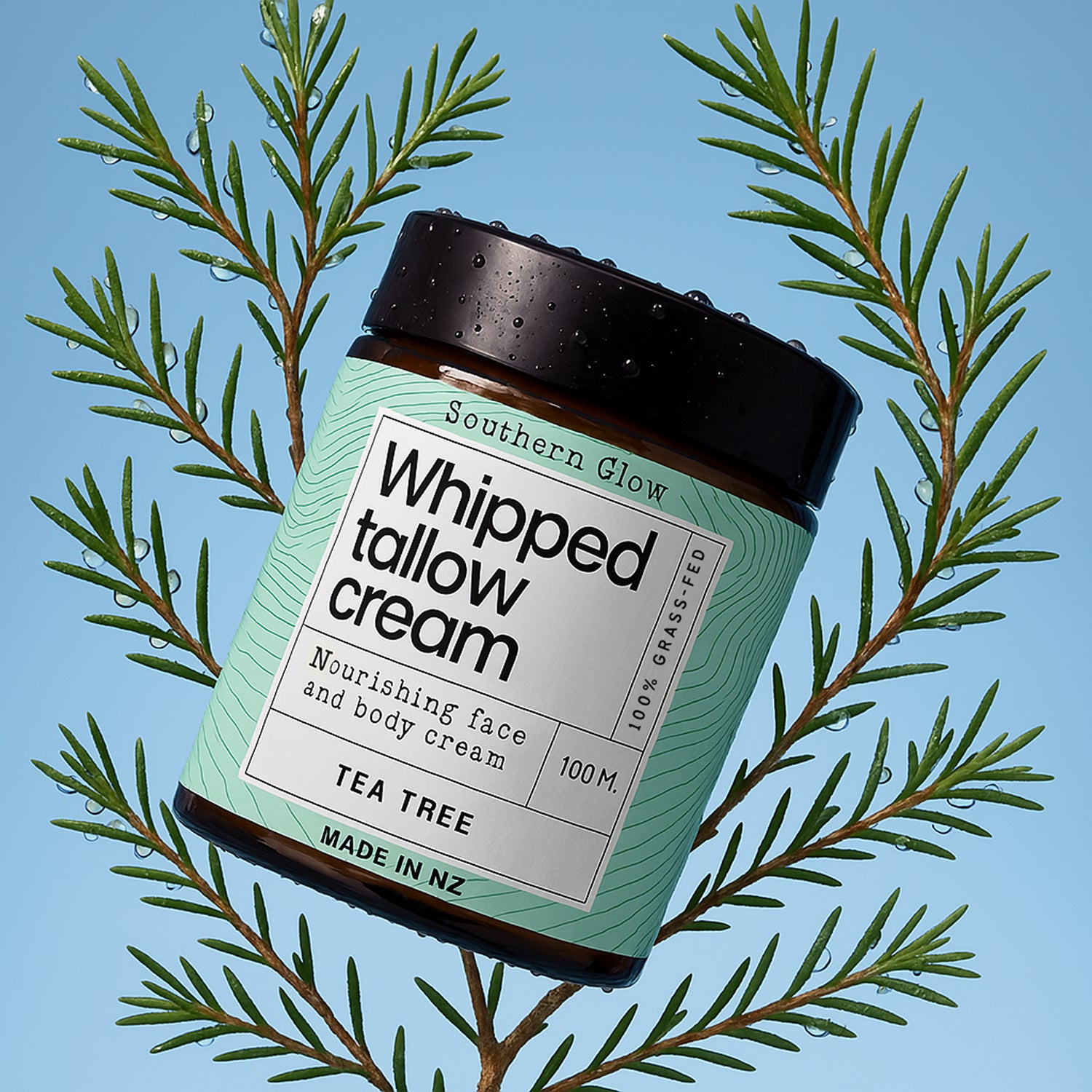 Jar of whipped tallow cream on tea tree leaves with a blue background